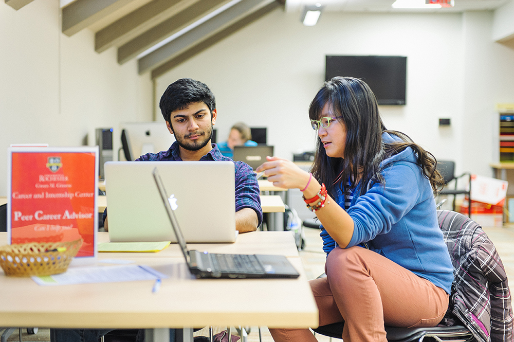 Two people sitting at a table with a laptop.