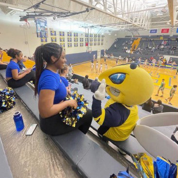 The student sitting with the mascot, Rocky on the bleachers.