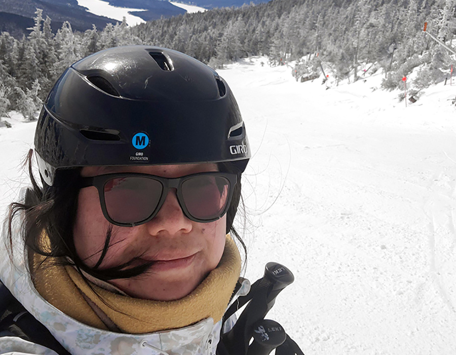 Alice wearing a helmet with a view of mountains in the background.