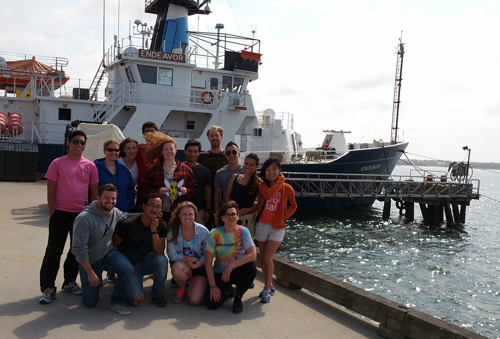 A group of people posing for the camera on a dock with a large ship behind them.