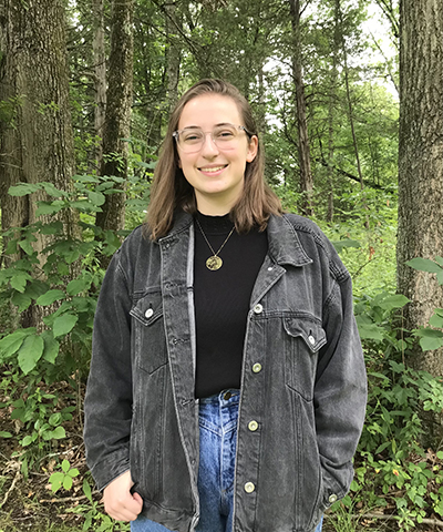 Katie Hall smiling at the camera with trees in the background.