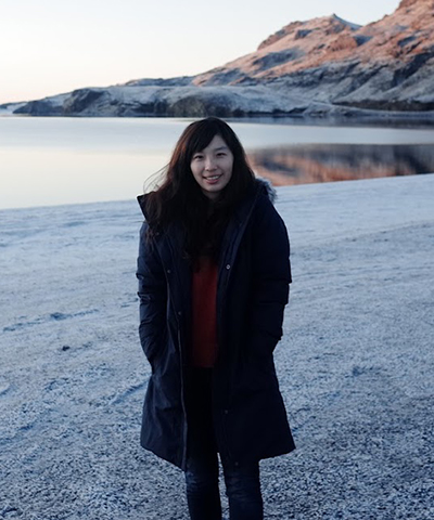 A smiling Hsin-Yu stands before a lake with mountains in the background.