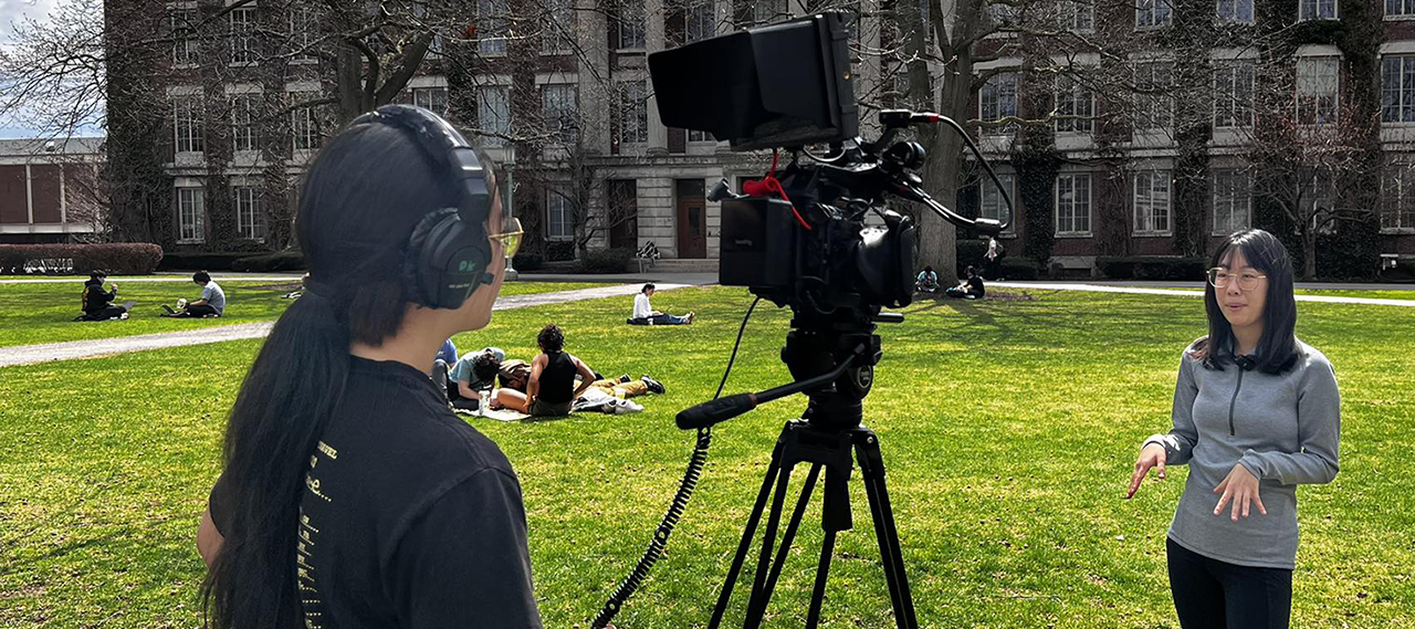Students on the quad on a sunny day filming a scene.