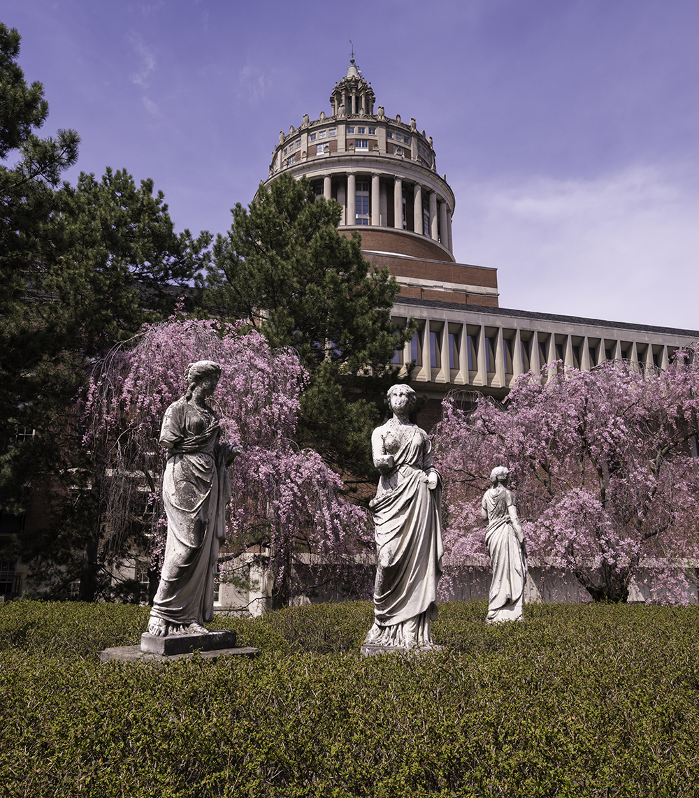 The four muses statues as seen in spring with Rush Rhees tower in the background.