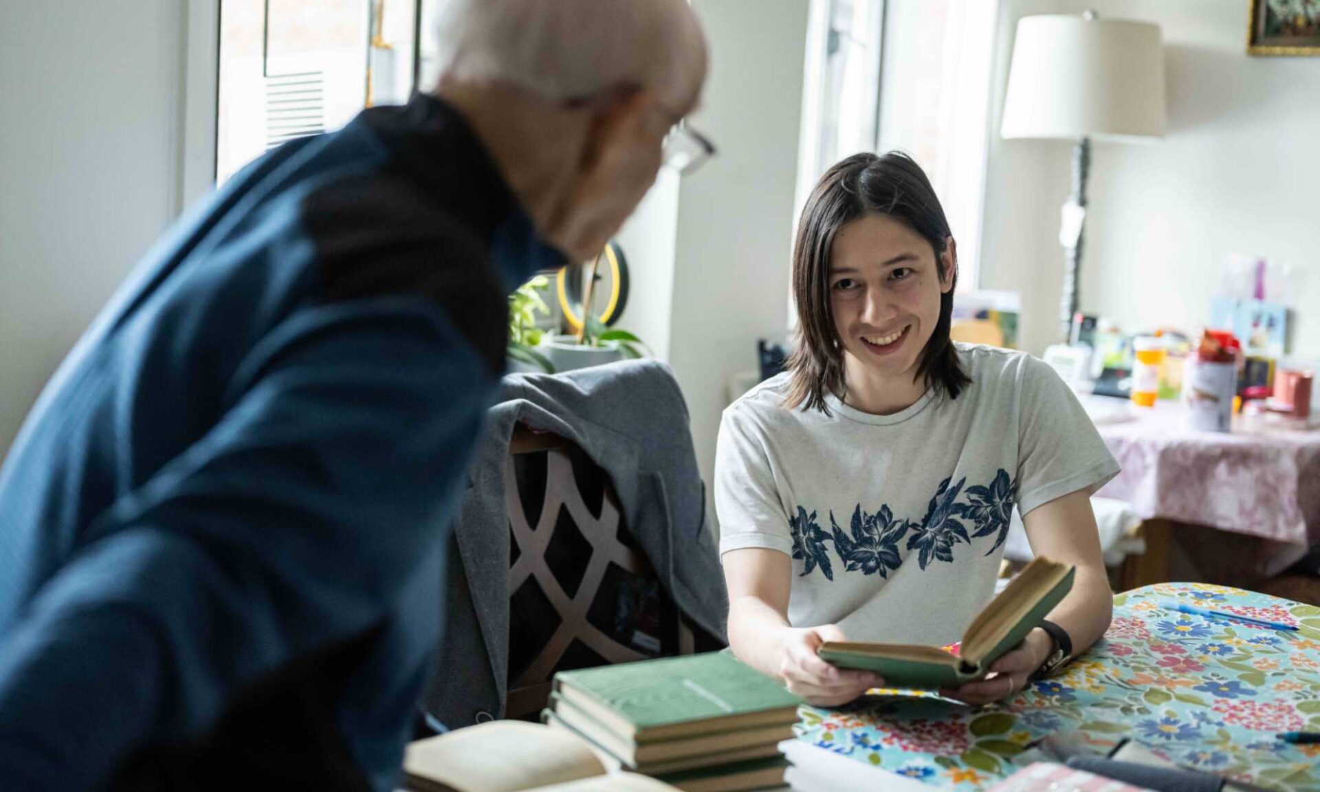 Aaron Do holds a poetry book and smiles while looking up at Yefim Ravin, who is seen from behind.