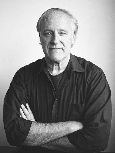 Harry Reis poses for the camera in a black and white photo with his arms folded.
