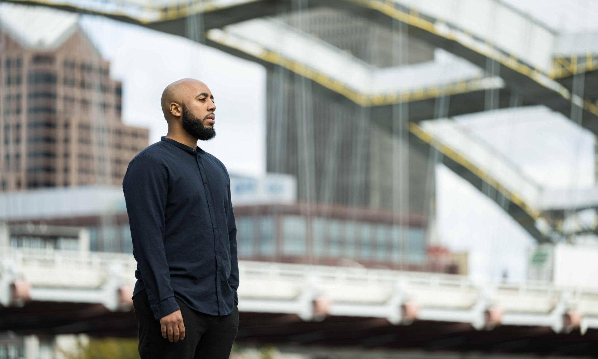 Philip V. McHarris, author of ‘beyond policing’, standing and looking off-camera framed by part of the frederick douglass–susan b. anthony memorial bridge in background.