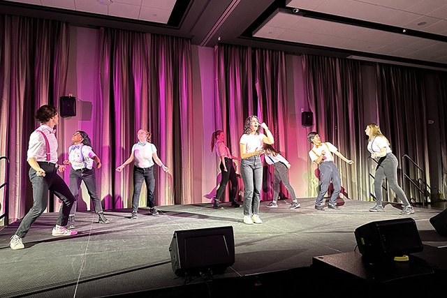 A group performs on stage with pink lighting.