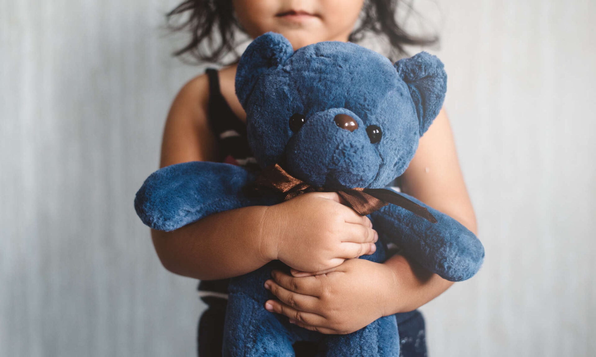 Close-up of a young girl holding a blue stuffed bear to illustrate child sexual abuse prevention.