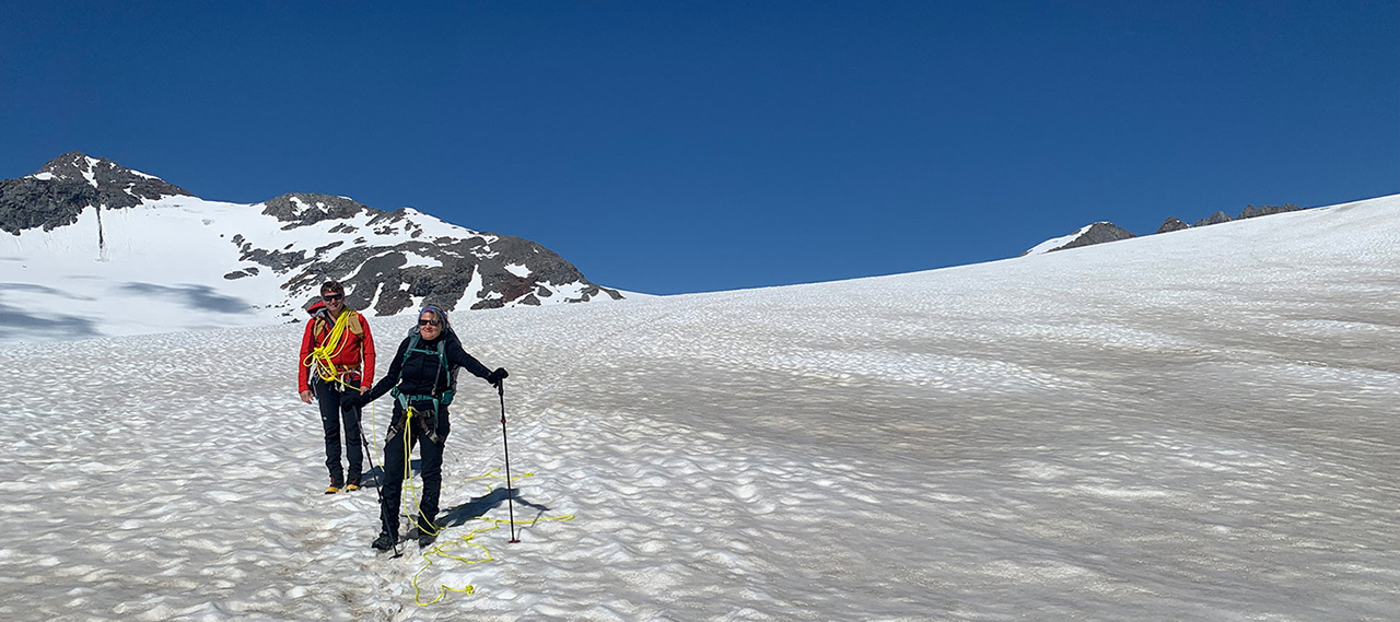 Two hikers in climbing gear pose for a photo on a glacier.