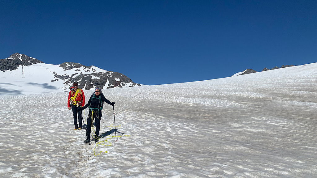 Two hikers in climbing gear pose for a photo on a glacier.