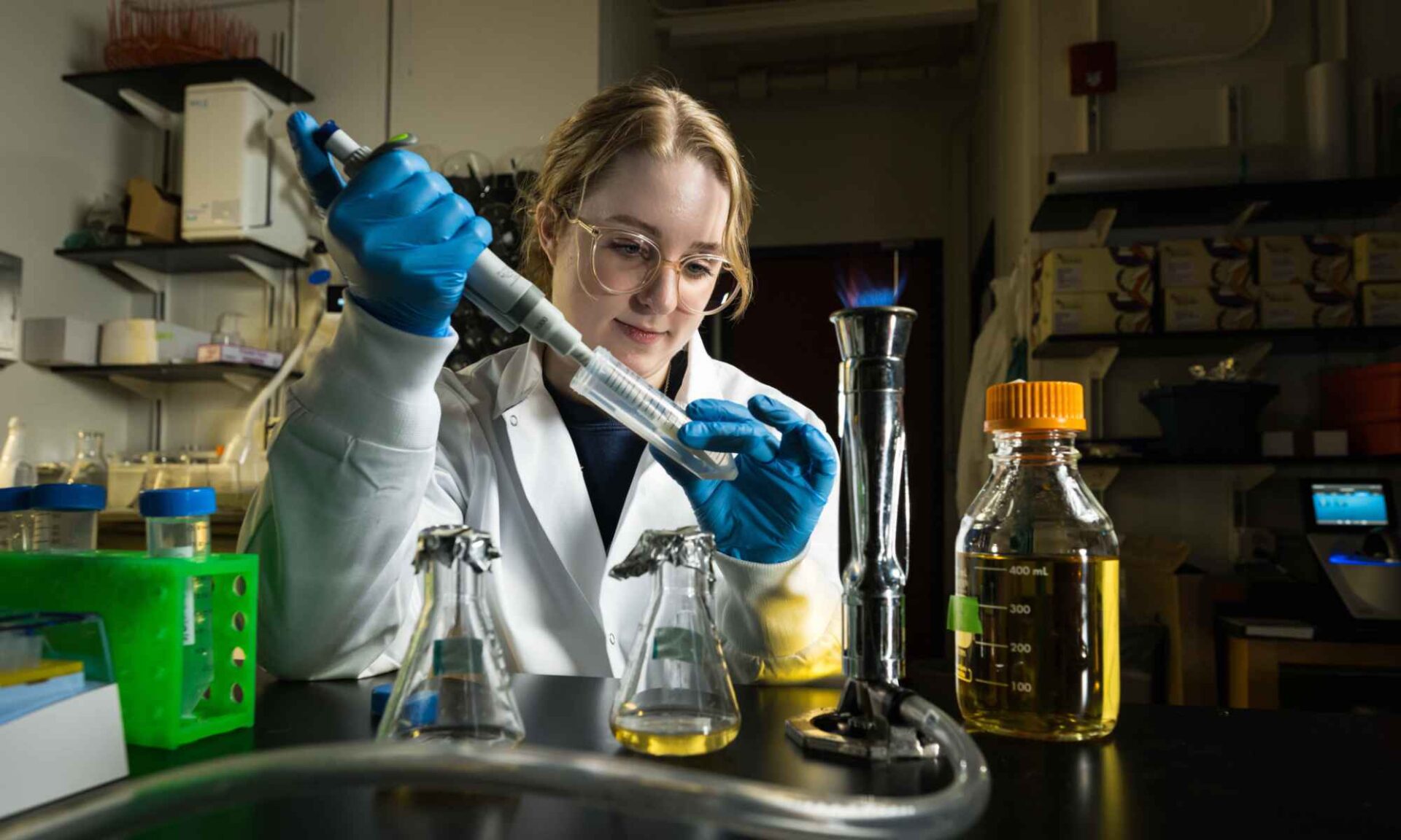 Student in a lab coat and safety gear pipes bacteria that will eventually form bioglass microlenses.