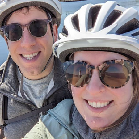 Emily wearing a bike helmet and smiling at the camera with another person in the background.