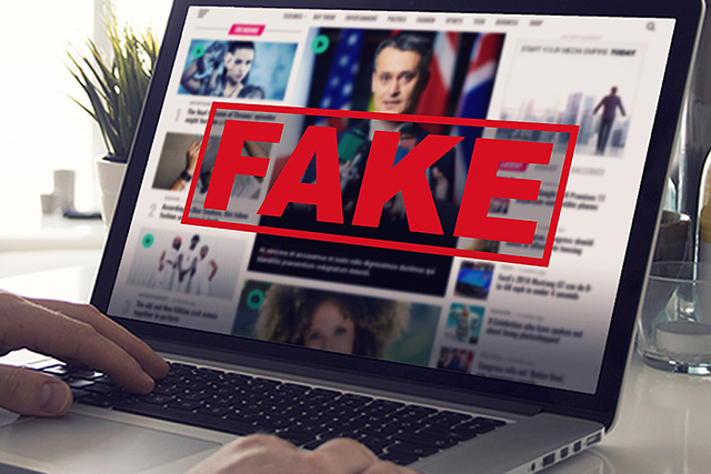 Hands using a laptop to scroll through a news feed with the word FAKE stamped across the screen.