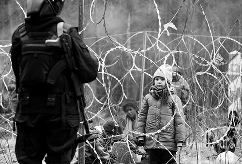 A still image from the film of a child staring at an adult through barbed wire fence.