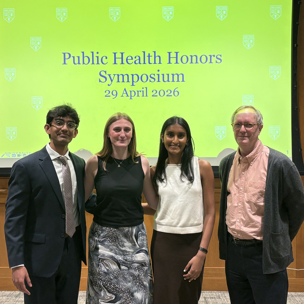 The three honors students pose with a professor in front of a projection screen.