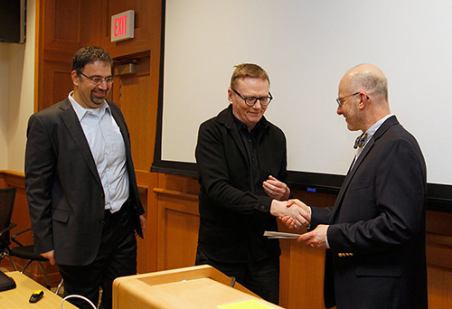 A man shaking hands with the award presenter while a third man looks on.